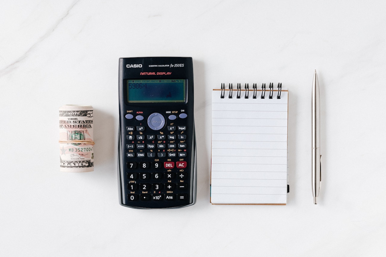 Una calculadora, una libreta con un boli y dinero para calcular cuánto tiene que facturar un autónomo para ganar 2000 €